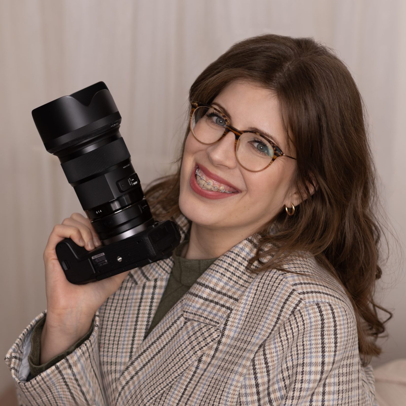 Az fotós, Sas-Kormos Evelin portréja, amin egy fényképezőgépet tart.