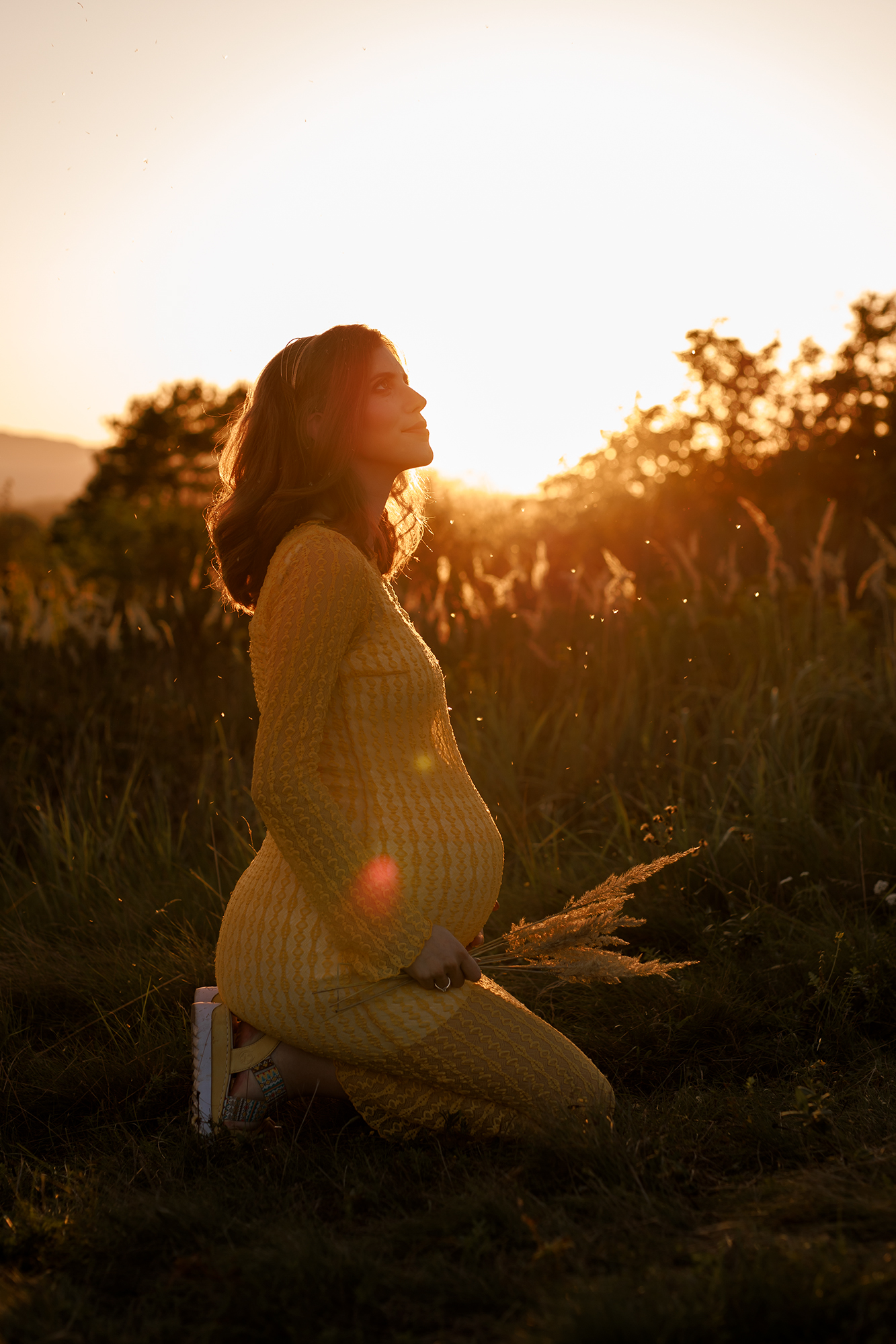kismama térdel kültéri fotózáson a naplementében, aranyórában