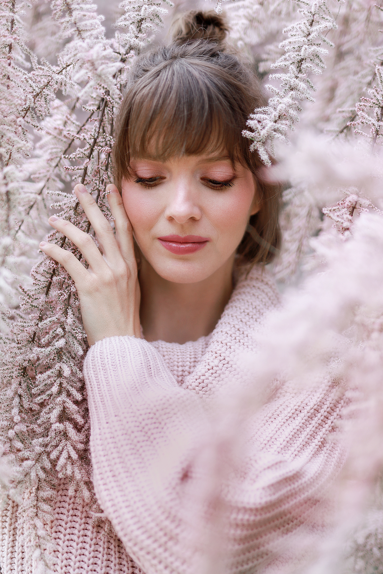 Fiatal nő a tavaszi virágok között mosolyogva pózol lecsukott szemmel.