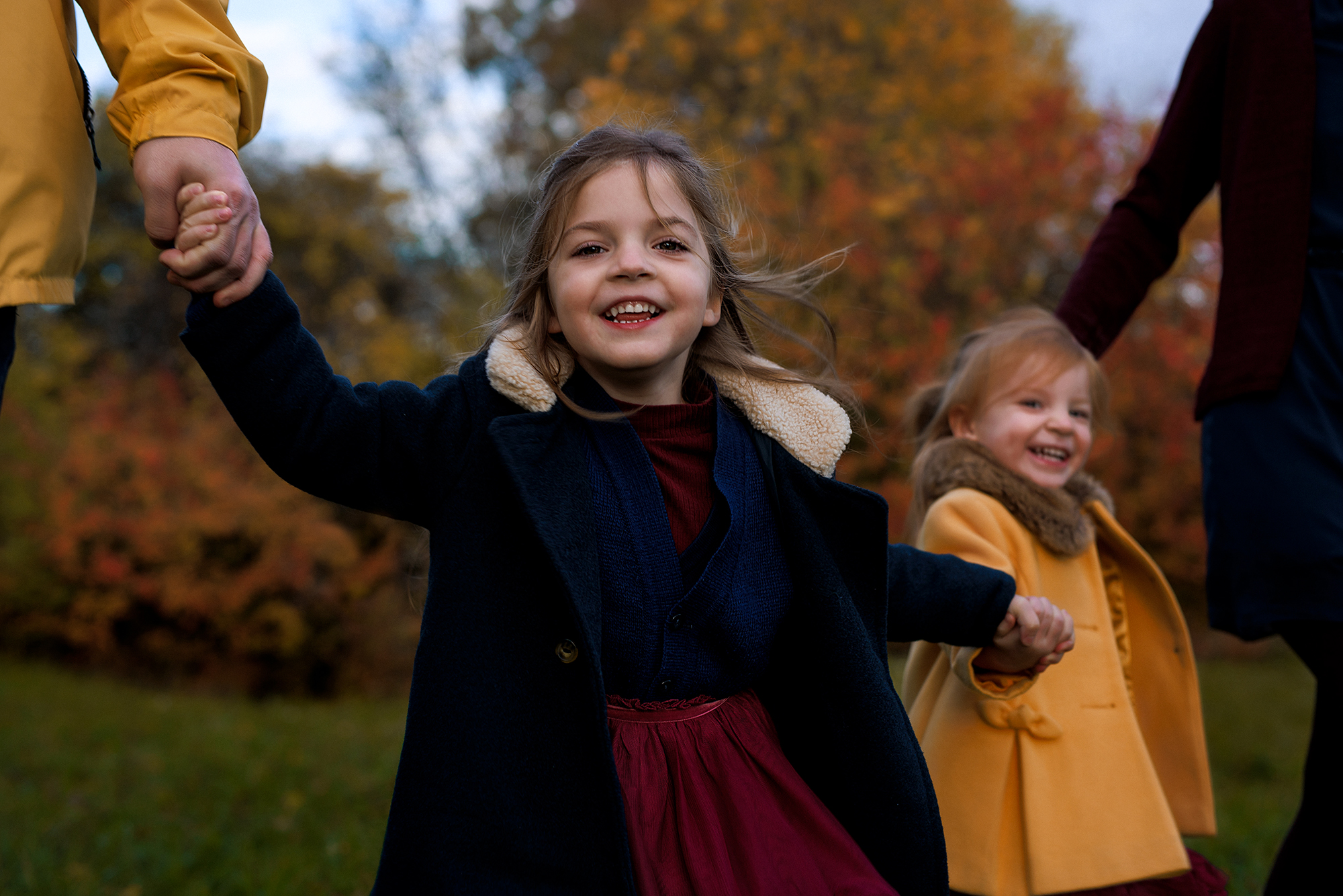 mosolygó kislányok fogják a szüleik kezét a kültéri fotózáson