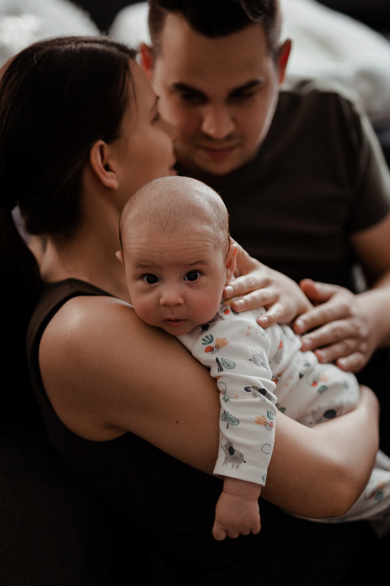 Családi fotón az anyuka öleli a kisbabát, aki a kamerába néz.