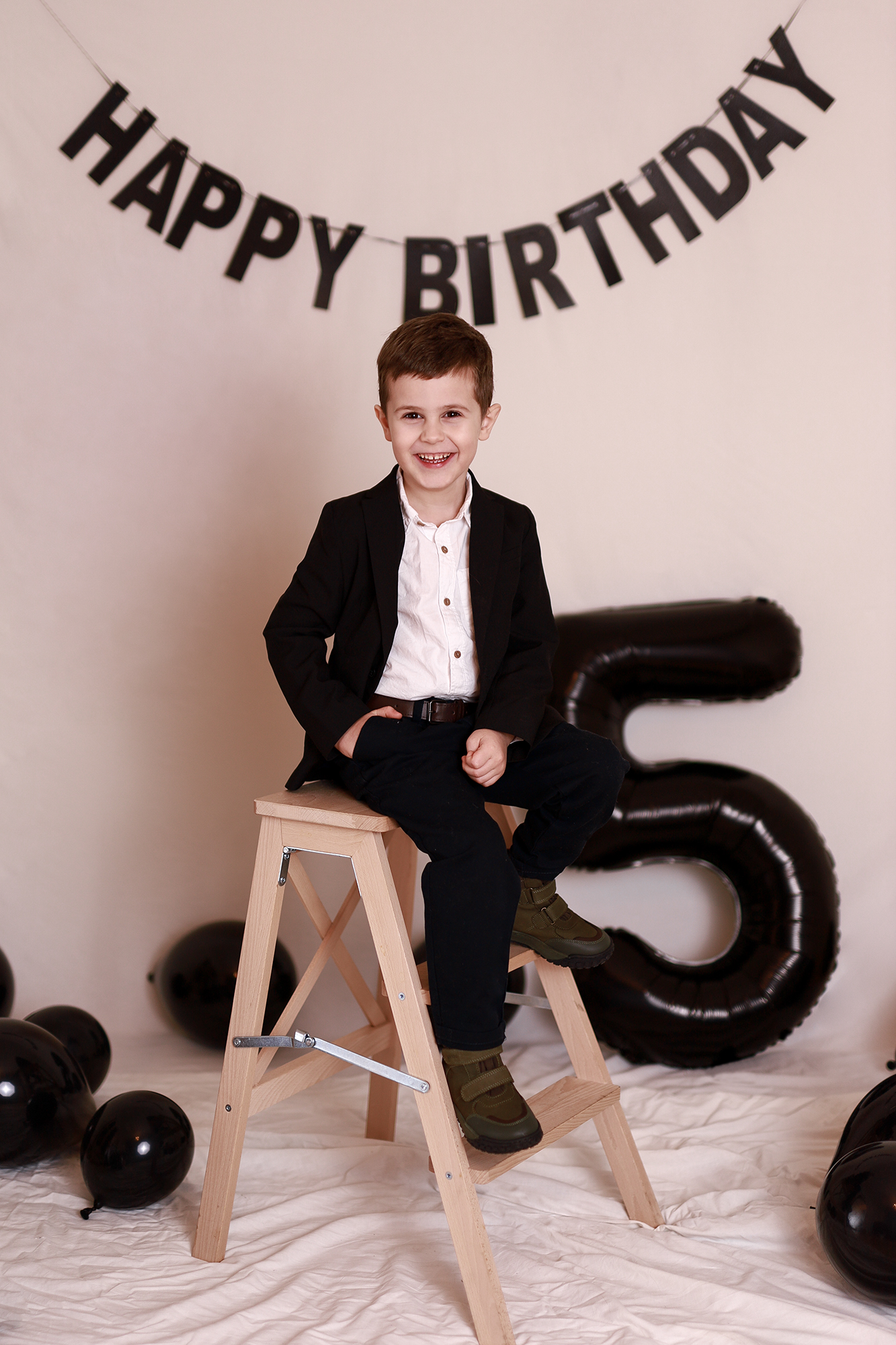 5 éves szülinapos kisfiú elegáns ruhában pózol fekete dekorban,