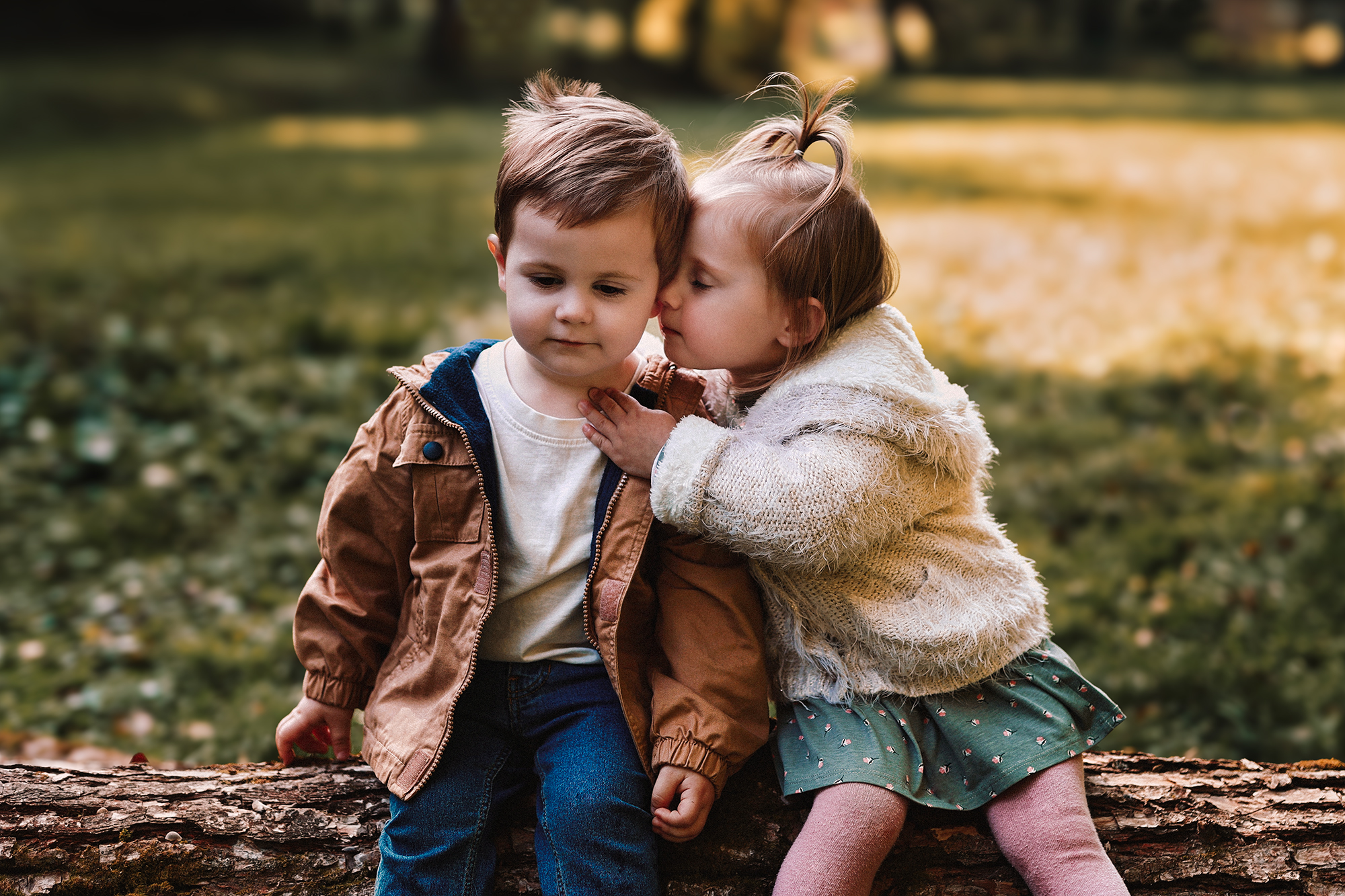Kislány puszit ad a kisfiúnak egy farönkön ülve