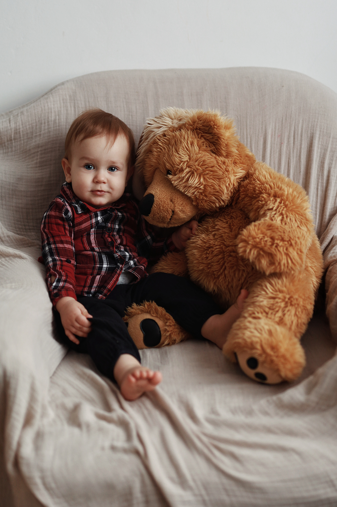 totyogó baba ül egy fotelben óriási macival